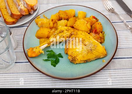 Gebackene Hühnerschenkel mit Bratensoße garniert mit Petersilie und gedünsteter Kartoffel und Karotte Stockfoto