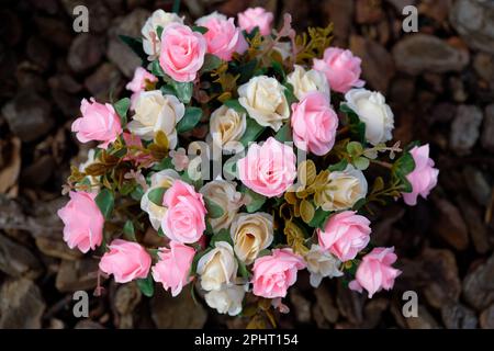 Strauß künstlicher rosa und beiger Rosen, von oben gesehen, auf dunklem, verschwommenem Boden Stockfoto