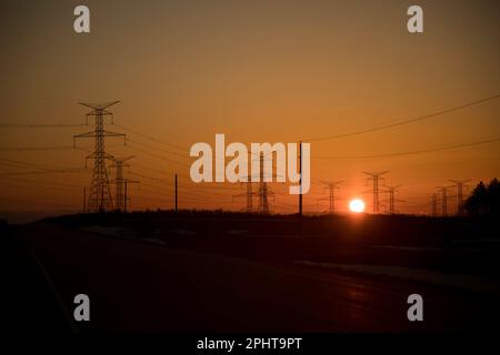 Powerlines und Pylonen sind Silhouetten gegen das Leuchten des Sonnenuntergangs Stockfoto