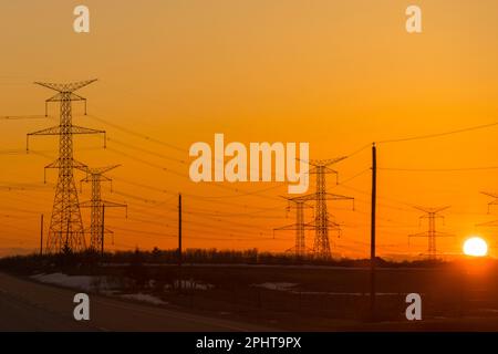 Powerlines und Pylonen sind Silhouetten gegen das Leuchten des Sonnenuntergangs Stockfoto