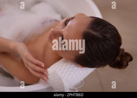 Junge Frau, die das Kissen benutzte, während sie ein Schaumbad im Innenbereich, von oben, genoss Stockfoto