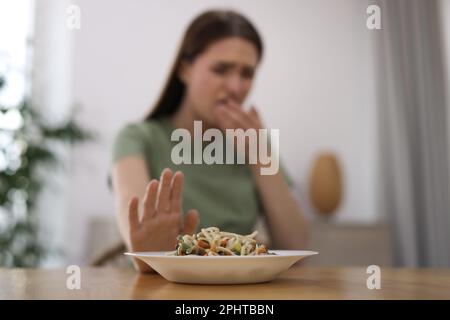 Junge Frau mit Übelkeit am Holztisch in Innenräumen, Schwerpunkt auf Essen Stockfoto