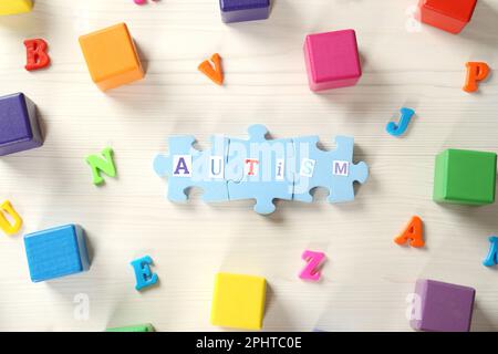 Wort Autismus aus Puzzleteilen, bunten Würfeln und Buchstaben auf weißem Holztisch, flach liegend Stockfoto
