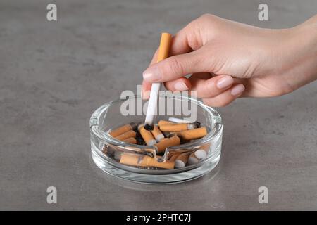 Eine Frau, die Zigaretten im Aschenbecher auf dem grauen Tisch ausmacht Stockfoto