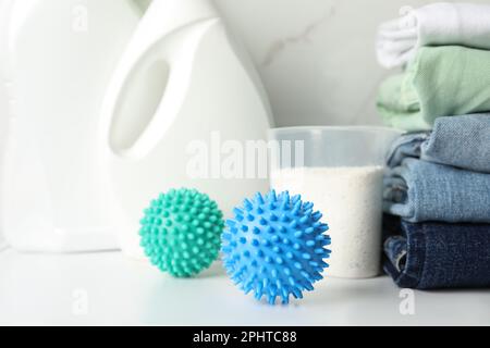 Trocknerkugeln, gestapelte saubere Kleidung und Reinigungsmittel auf dem weißen Tisch Stockfoto