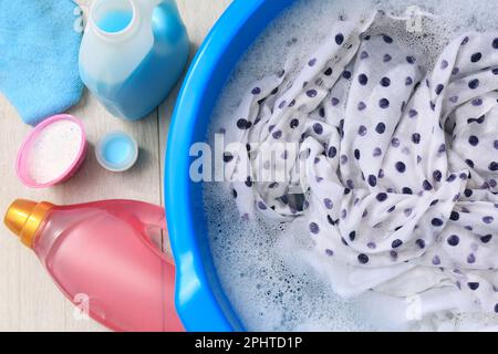 Waschbecken mit Kleidungsstücken in Sud neben Flaschen mit Waschmitteln und Pulver auf dem Boden, flach liegend. Wäsche waschen Stockfoto