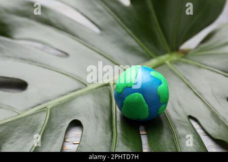 Frohen Tag Der Erde. Planet aus Plastik auf grünem Blatt, Platz für Text Stockfoto