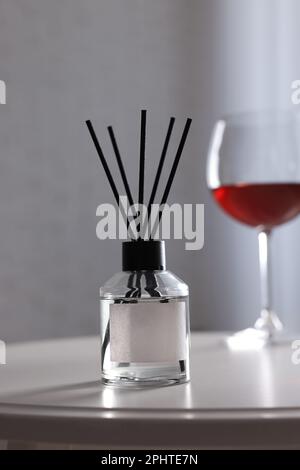 Reed-Diffusor und Glas Wein auf weißem Tisch im Innenbereich Stockfoto