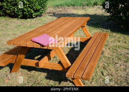 Gefaltete rot-weiße Tischdecke mit Karomuster auf einem Holzpicknicktisch im Park Stockfoto