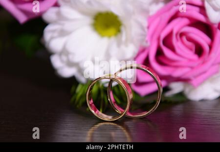 Goldene Eheringe auf einem schwarzen Tisch auf einem farbigen Hintergrund. Hochwertiges Foto Stockfoto