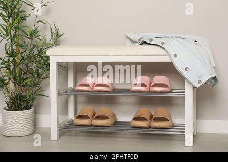 Elegante Aufbewahrungsbank mit verschiedenen Paar Gummipantoffeln und wunderschönen Zimmerpflanzen in der Nähe der weißen Wand im Flur Stockfoto
