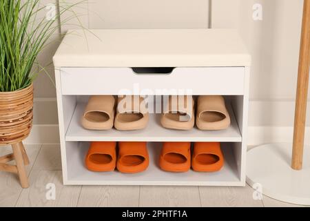 Elegante Aufbewahrungsbank mit verschiedenen Paar Gummipantoffeln und wunderschönen Zimmerpflanzen in der Nähe der weißen Wand im Flur Stockfoto