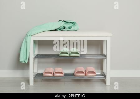 Elegante Aufbewahrungsbank mit verschiedenen Paar Gummipantoffeln an der weißen Wand im Flur Stockfoto