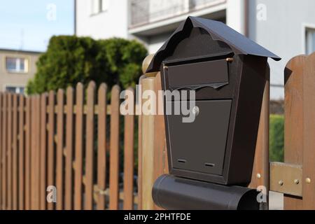 Wunderschöner, hausförmiger Briefkasten mit Zeitungshalter auf Holzzaun im Freien, Platz für Text Stockfoto