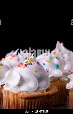 Flauschige Vanille-Cupcakes mit Baiser und Dragees auf schwarzem Hintergrund, Originalrezept Stockfoto