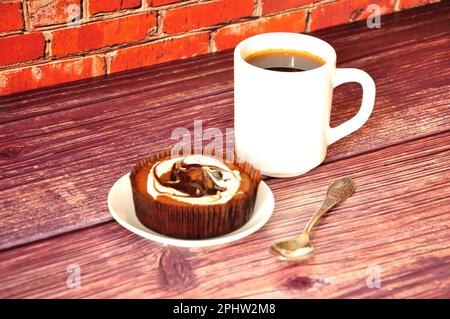 Schokoladentörtchen mit Proteincreme und eine Tasse heißer schwarzer Kaffee auf einem Holztisch. Nahaufnahme. Stockfoto