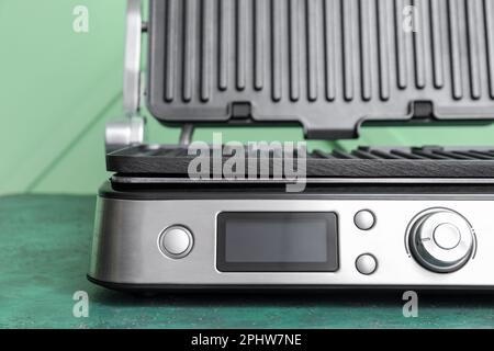 Moderner elektrischer Grill mit offenem Deckel auf grünem Tisch Stockfoto