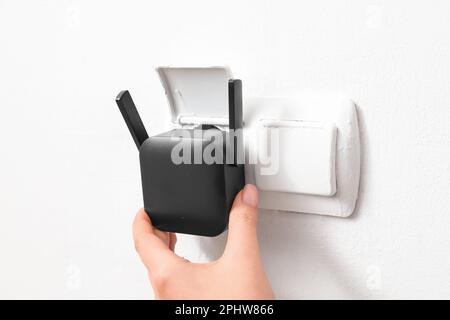 Frau, die den schwarzen WLAN-Repeater in die Steckdose an der weißen Wand einsteckt Stockfoto