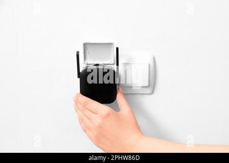 Frau, die den schwarzen WLAN-Repeater in die Steckdose an der weißen Wand einsteckt Stockfoto