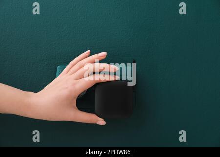 Frau, die den schwarzen WLAN-Repeater in die Steckdose an der grünen Wand steckt Stockfoto
