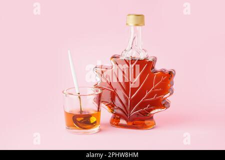 Flasche und Löffel in einem Glas leckeren Ahornsirups auf rosa Hintergrund Stockfoto