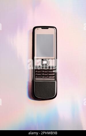 Altes Handy mit holografischem Hintergrund. Retro-, Vintage- und Nostalgie-Stil. Y2K-Design-Trend Stockfoto