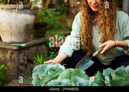 Junge, weiße Gärtnerin, die Gemüse pflanzt und ein glückliches Lächeln aus der Nahaufnahme macht. Junge, fröhliche Frau mit Kelle in ihrem Garten, die sich um sie kümmert Stockfoto