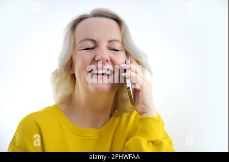 Porträt einer attraktiven, fröhlichen, grauhaarigen Frau, die auf einem Diwan sitzt und auf dem Handy telefoniert, im Haus, in der Wohnung. Hochwertiges Foto Stockfoto