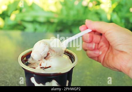 Von Hand schaufelnde, schmelzende Vanille-Softeis mit Löffel Stockfoto