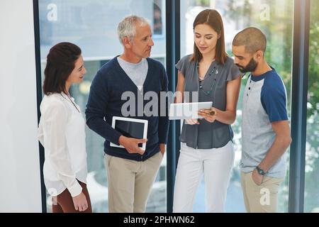 Reden wir über die Arbeit. Eine Gruppe von Kollegen, die sich über ein Tablet in ihrem Büro unterhalten. Stockfoto