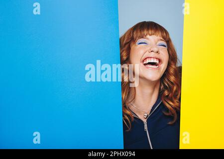 Junge Frau, die lacht, während sie mit zwei geometrischen Formen steht. Eine Frau, die Spaß in einem Designstudio hat. Stockfoto