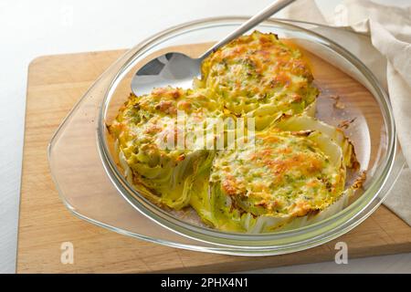 Gebackene Scheiben Chinakohl oder napakohl in einem Glasauflauf auf einem hölzernen Küchenbrett, kreatives vegetarisches Gericht, Kopierraum, ausgewählter Fokus, schmales d Stockfoto