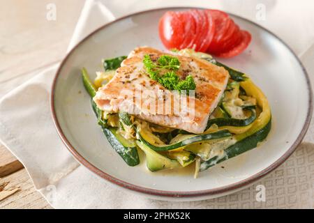 Gebratener Wildlachs mit Petersilie-Garnierung auf Zucchini-Gemüse und frische Tomaten auf einem leichten Teller, gesunde Mahlzeit für eine kohlenhydratarme Diät, ausgewählter Schwerpunkt, nar Stockfoto