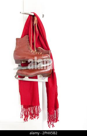 Rote Oldtimer-Schlittschuhe und roter Schal, der auf dem weißen Türhintergrund hängt Stockfoto