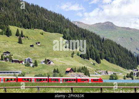 Davos, Schweiz - Juni 24. 2021: Ein roter Passagier-Expresszug von Rhatian Railway Company überquert den wunderschönen Davos-See, Grison, SWI Stockfoto