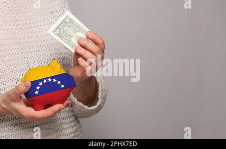 Flagge Venezuelas auf einer Geldbank in venezolanischen Frauenhänden. Punkte, Pensionsfonds, Armut, Wohlstand, Altersvorsorge Stockfoto