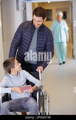 Vater spielt, wie er sich im Rollstuhl um seinen Sohn kümmert Stockfoto