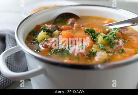 Eintopf mit Karotten, Kartoffeln und geräuchertem Schweinefleisch in einem weißen Emaille-Topf. Stockfoto