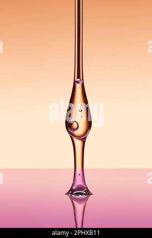 Ein Tropfen feuchtigkeitsspendendes Serum oder ätherisches Öl aus einer Pipette. Auf abgestuftem beigefarbenem und rosafarbenem Hintergrund. Stockfoto