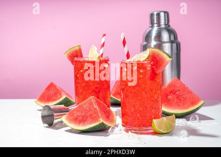 Cocktail aus Wassermelonen-Limonade mit Limette und in Scheiben geschnittener Wassermelone auf einem trendigen, hochfarbigen, weiß-rosa Hintergrund Stockfoto