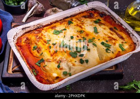 Hausgemachte Cannelloni-Pasta, großes Tablett mit gebackenen Cannelloni mit Hackfleisch mit Béchamel-Sauce, mit Kräutern in Zutaten auf dunklem Hintergrund Stockfoto