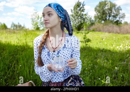 Frau mit transparenter Teekanne. Sammelt frische grüne Kräuter, ernten und machen gesunden Tee. Verschwommenes Bild, selektiver Fokus Stockfoto