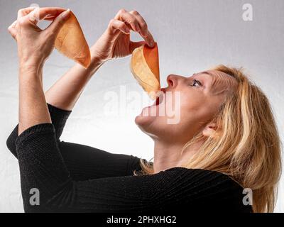 Eine weiße Frau hält eine Scheibe rohen italienischen Schinken in jeder ihrer beiden Hände und bereitet sich darauf vor, sie unersättlich zu essen Stockfoto
