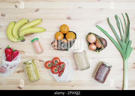 Gemüse und Obst in wiederverwendbaren Beuteln und Müsli, Hülsenfrüchte, Pasta in Glasgefäßen auf einem Holztisch. Das Konzept der Abfallvermeidung und der umweltfreundlichen Lebensweise Stockfoto