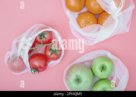 Apfel, Tangerinen und Tomaten in wiederverwendbaren Einkaufstaschen auf pinkfarbenem Hintergrund. Das Konzept der Abfallvermeidung und des umweltfreundlichen Lebensstils. Kein Plastik. Obere V-Achse Stockfoto