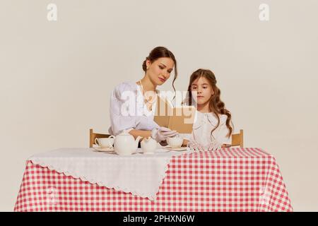 Porträt einer jungen, charmanten Frau, die ihre Tochter beim Lesen vor hellem Hintergrund unterrichtet Stockfoto