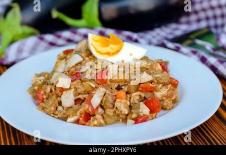 Gebratener Auberginen-Salat mit Tomaten und Ei auf einem Teller Stockfoto