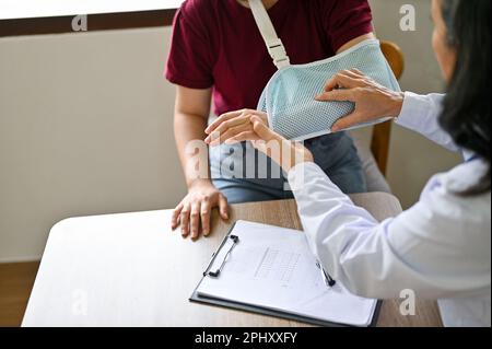 Eine Patientin mit gebrochenem Arm wird von einem Orthopäden-Arzt im Untersuchungsraum eines Krankenhauses untersucht und diagnostiziert. Stockfoto