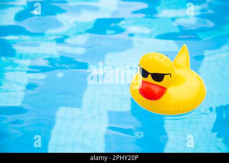 Im Pool schwimmender aufblasbarer Entenring. Gelbe Plastikente mit Sonnenbrille Stockfoto