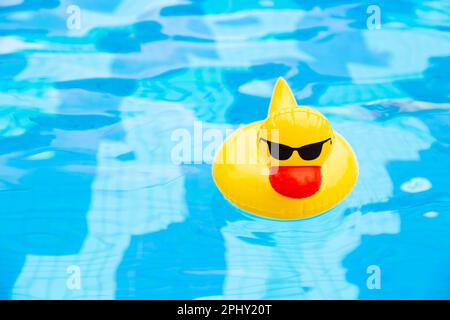 Im Pool schwimmender aufblasbarer Entenring. Gelbe Plastikente mit Sonnenbrille Stockfoto